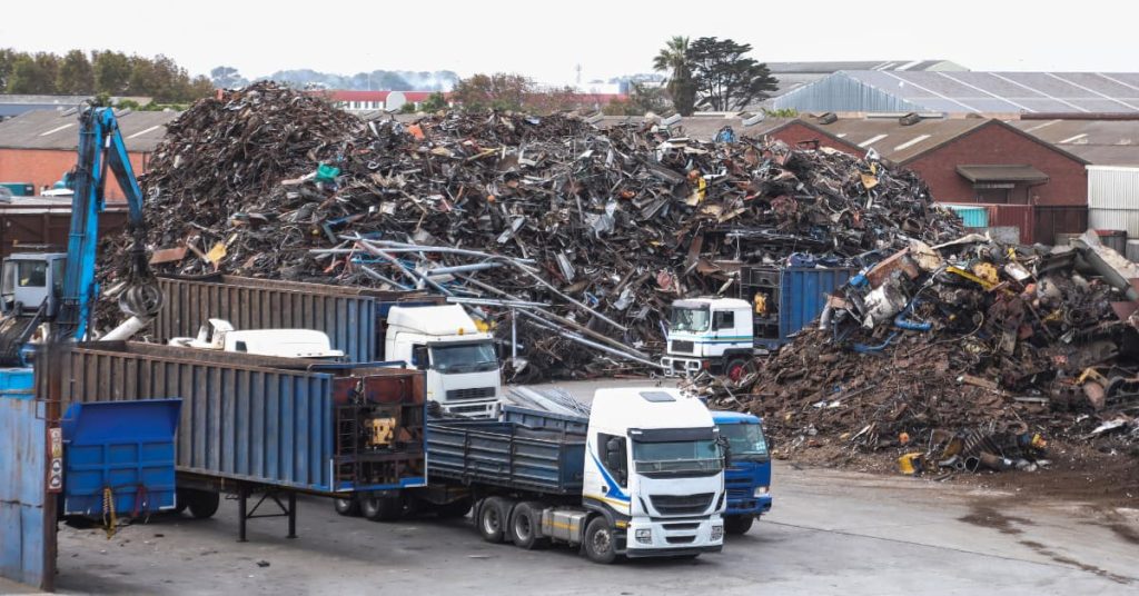 Planta de reciclaje de metales con camiones y maquinaria industrial, ejemplo de responsabilidad social y ambiental empresarial aplicada a la gestión sostenible de residuos.